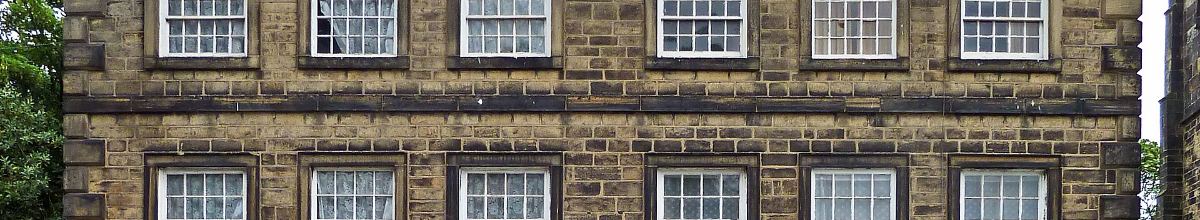 The stone frontage of a Georgian building with two ranks of white-framed sash windows and a moulded string course.