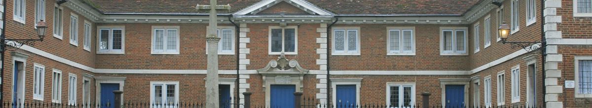 A symmetrical brick courtyard building with a stone-dressed centrepiece, blue doors and iron railings.